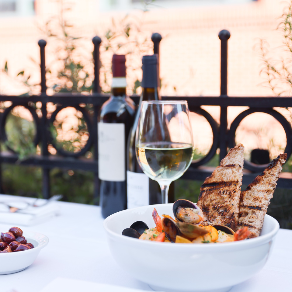 A Mediterranean seafood dish with grilled bread, wine, and olives on an outdoor table.