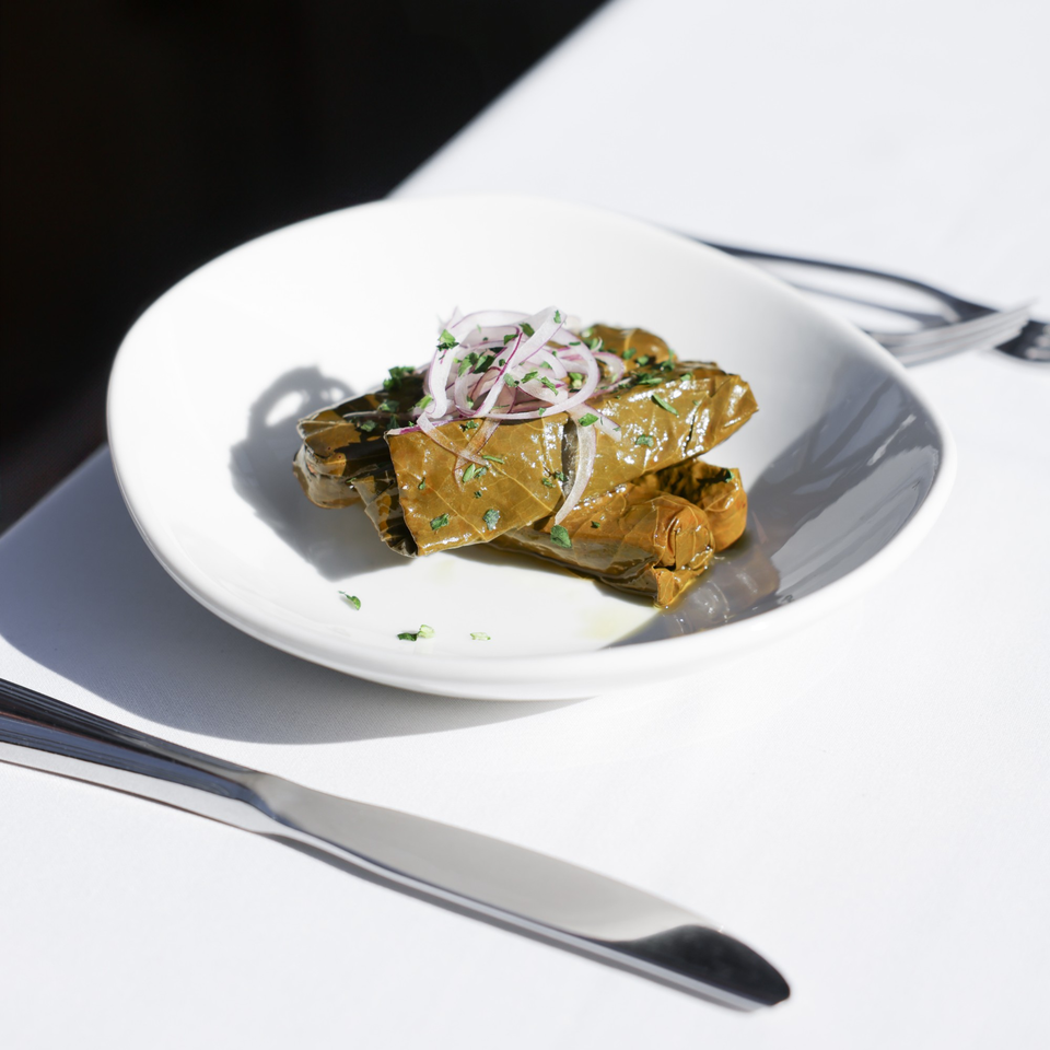 Mediterranean dolmades, grape leaves stuffed with rice and herbs, topped with red onion and parsley.