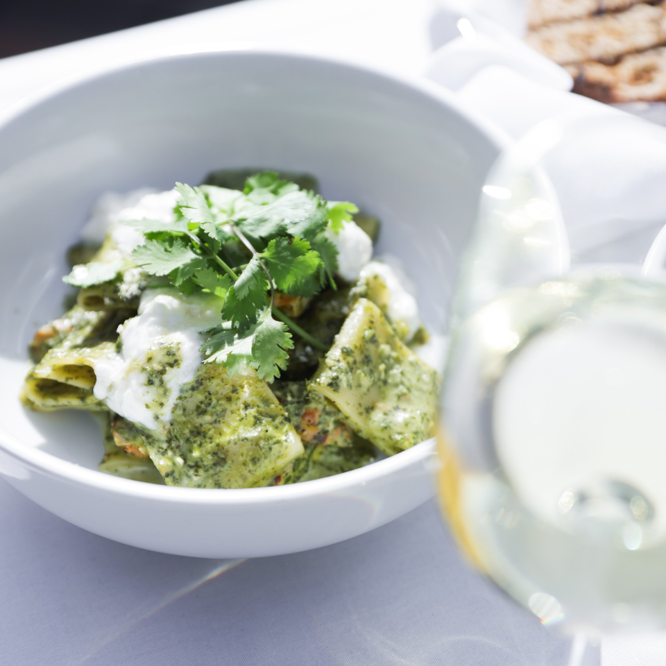 Mediterranean pasta with pesto, fresh mozzarella, and cilantro, next to a glass of white wine.