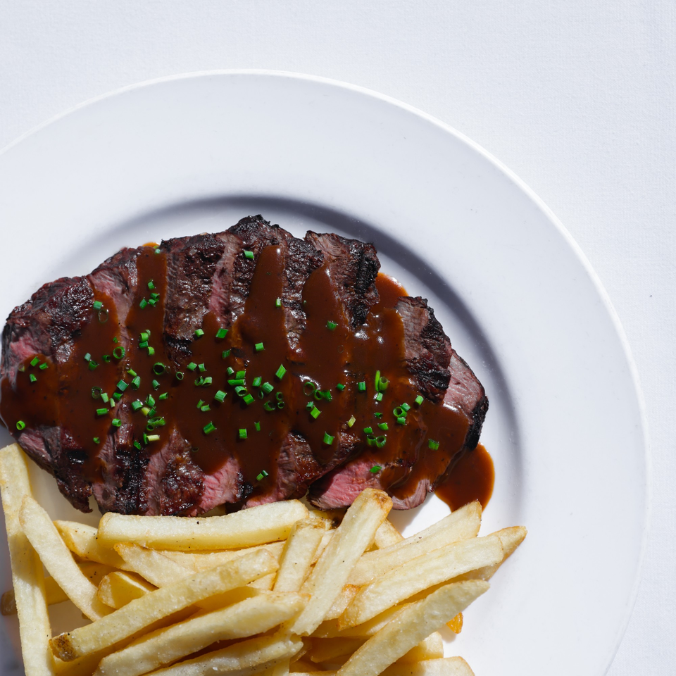 Sliced steak with brown sauce and chives, served with golden french fries on a white plate.