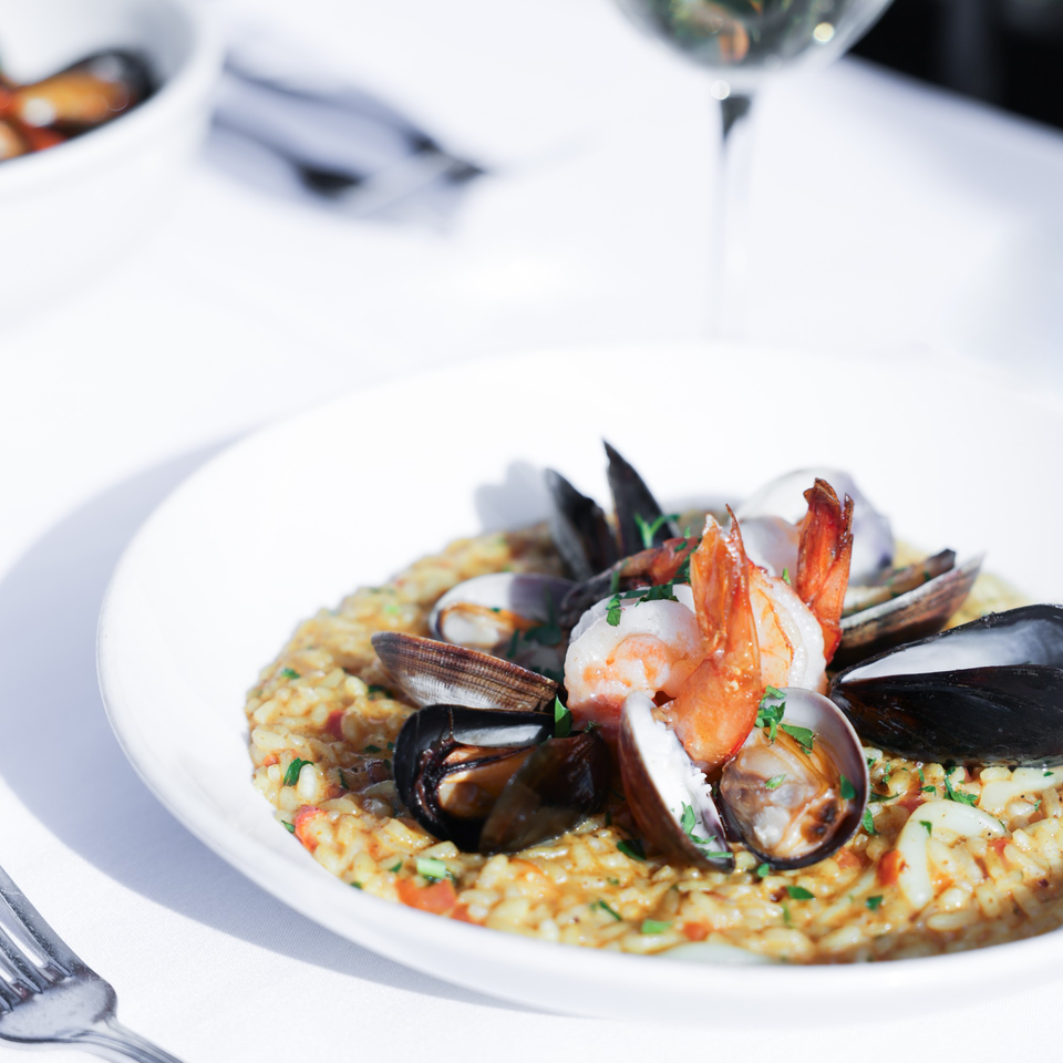 Seafood risotto with shrimp, mussels, and clams, garnished with parsley on a white plate.